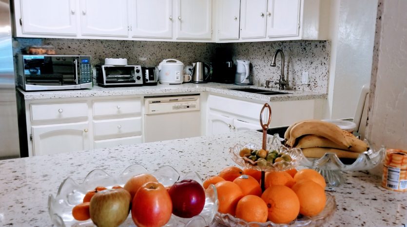 A kitchen with white cabinets and counters, apples in the foreground.