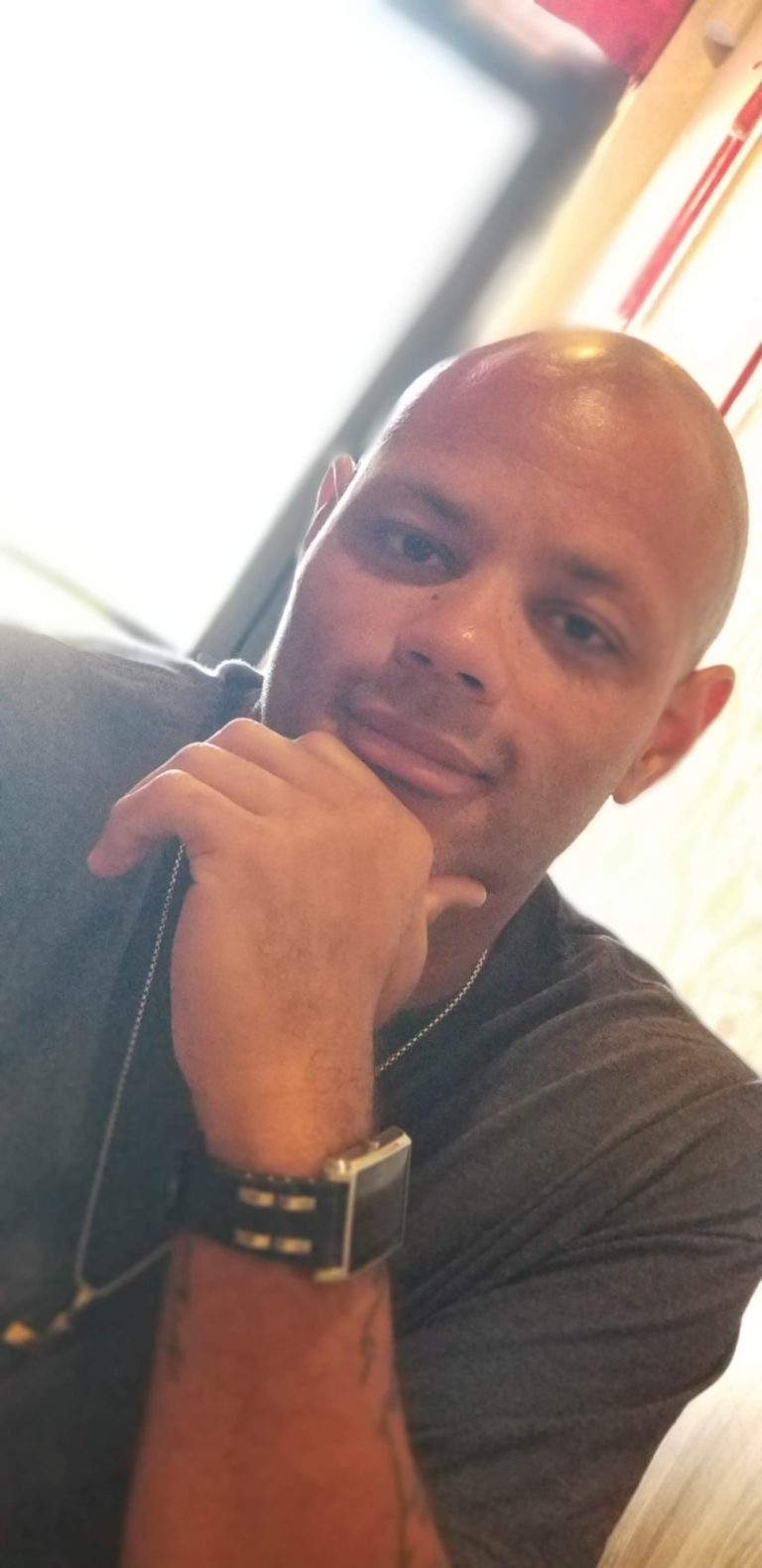 A bald man with his chin resting on his hand.