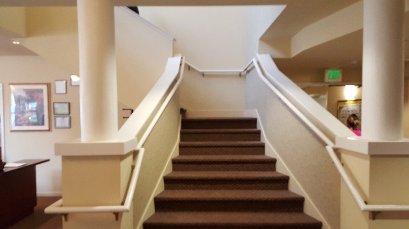 A staircase with brown carpet and white railing.