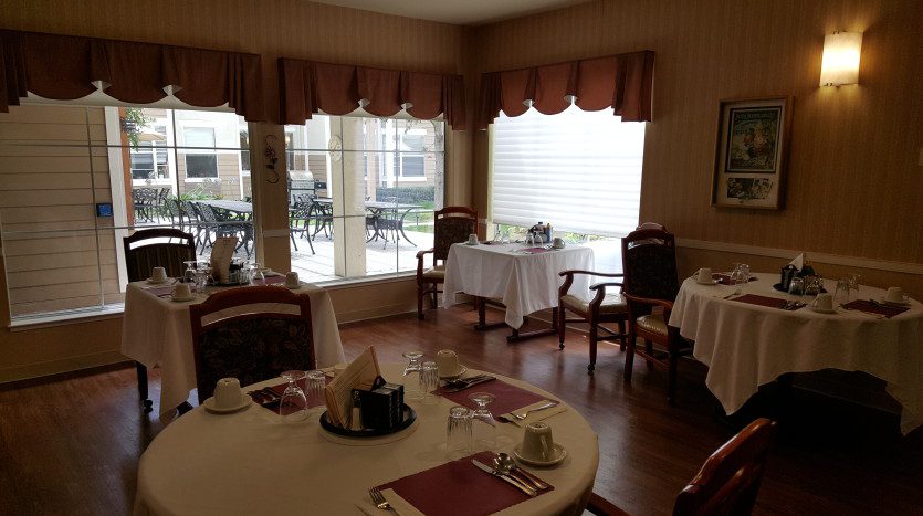 A dining room with tables and chairs, a table cloth, and a window.