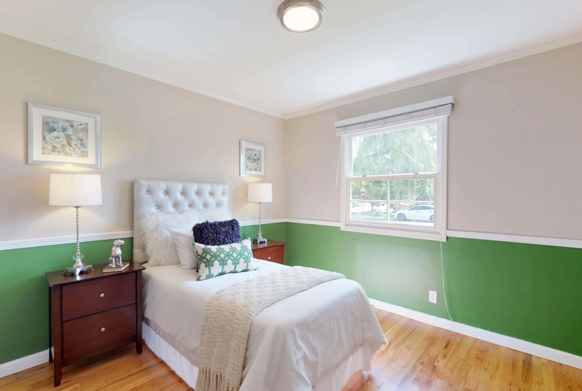 A bedroom with green and white walls, wooden floors and a bed.