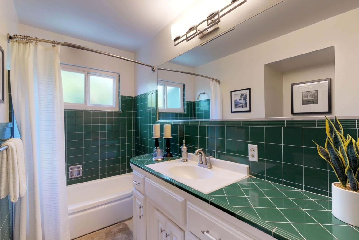 A bathroom with green tile and white cabinets.