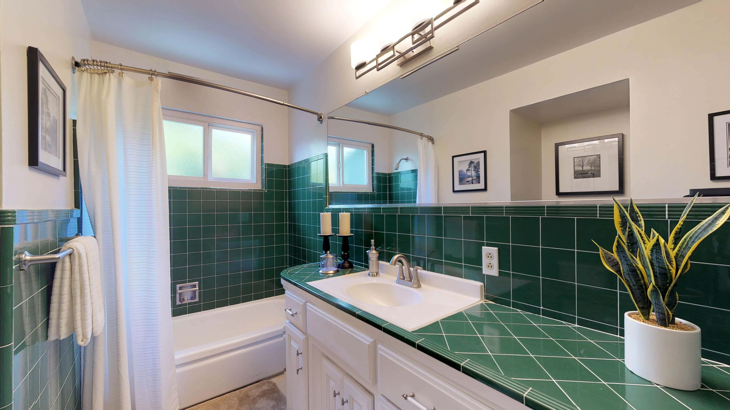 A bathroom with green tile and white cabinets.