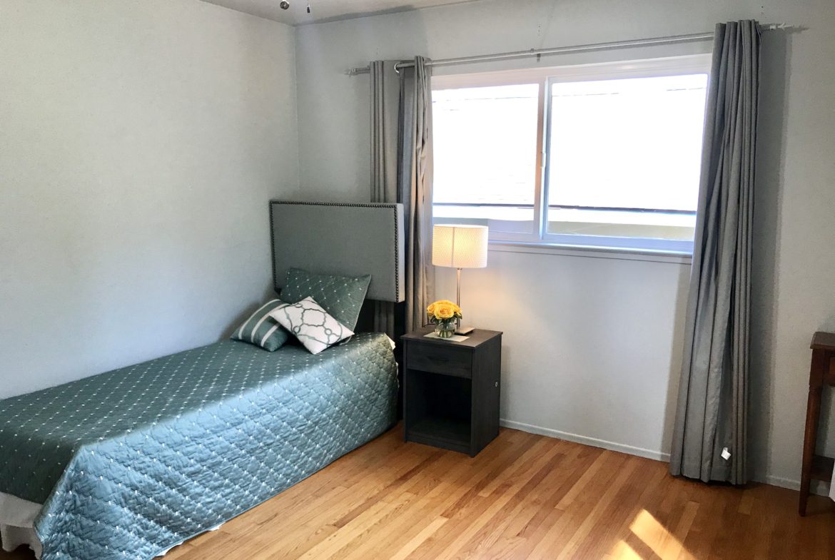 A bedroom with a bed, nightstand and window.