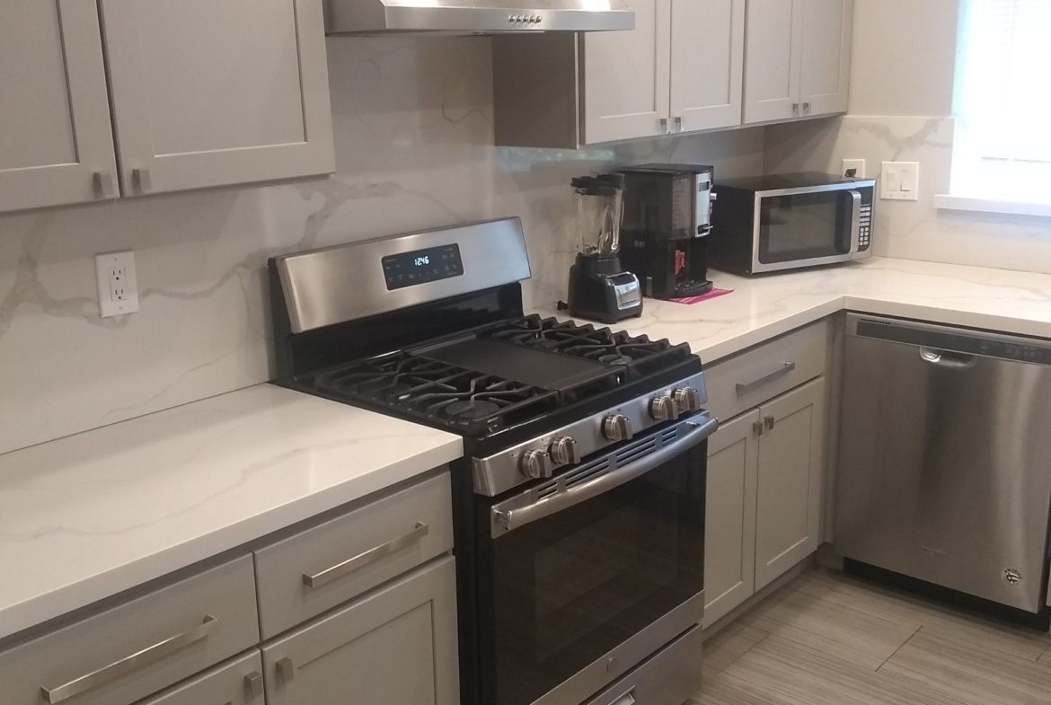 A kitchen with grey cabinets and white counters.