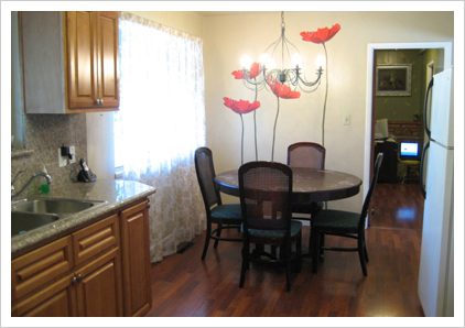 A dining room with a table and chairs, a window and some flowers on the wall.