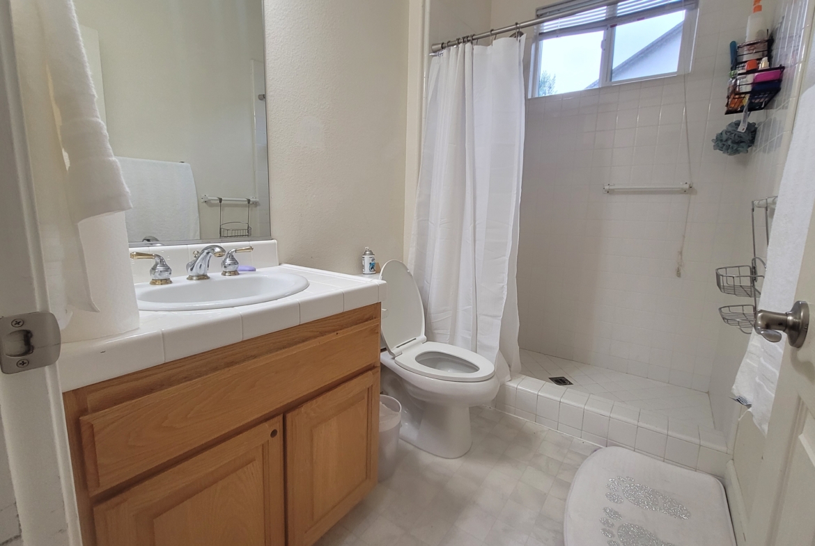 A bathroom with white tile and wood cabinets.