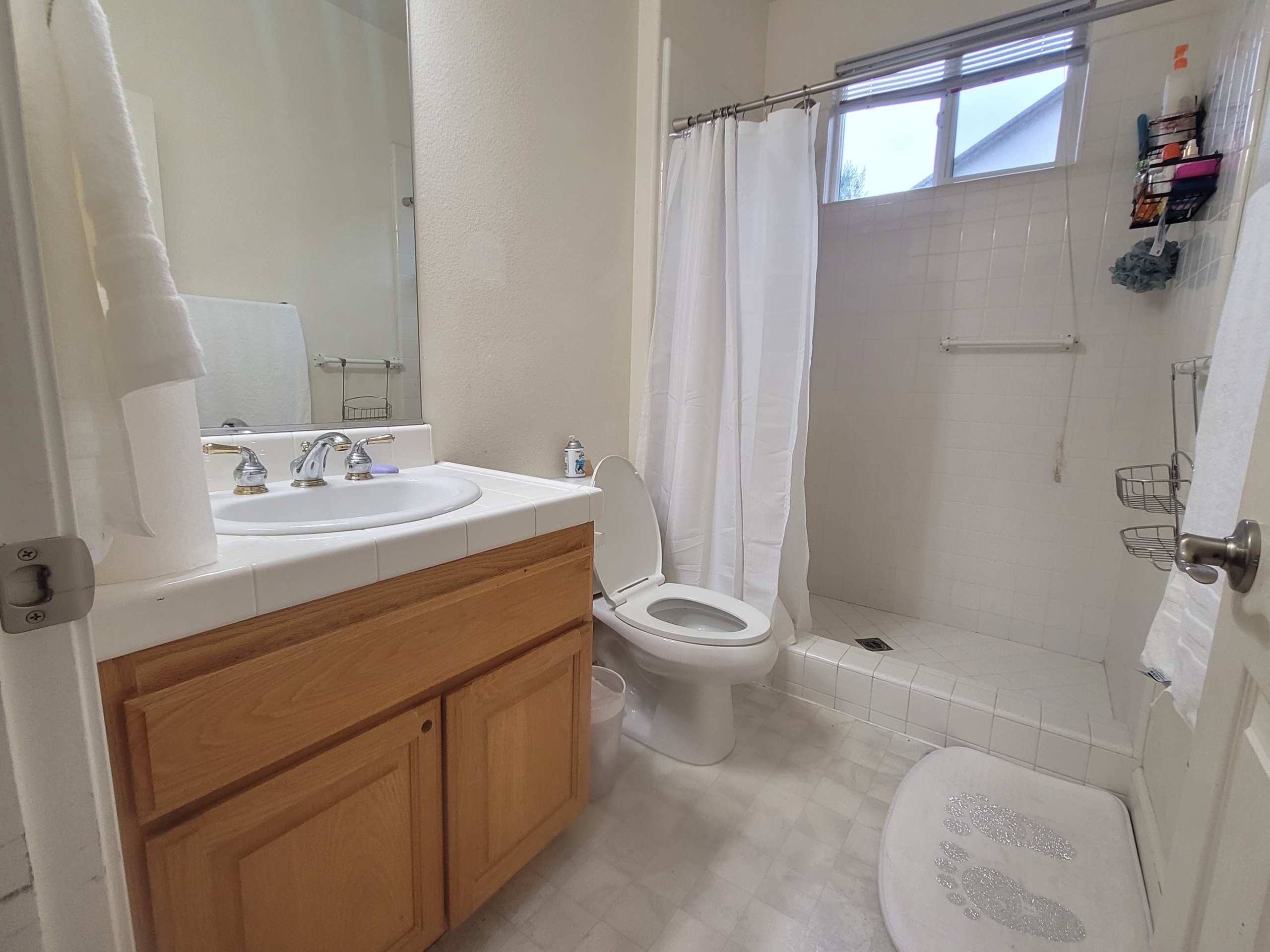 A bathroom with white tile and wood cabinets.