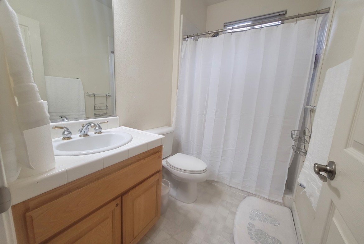 A bathroom with white tile and wood cabinets.