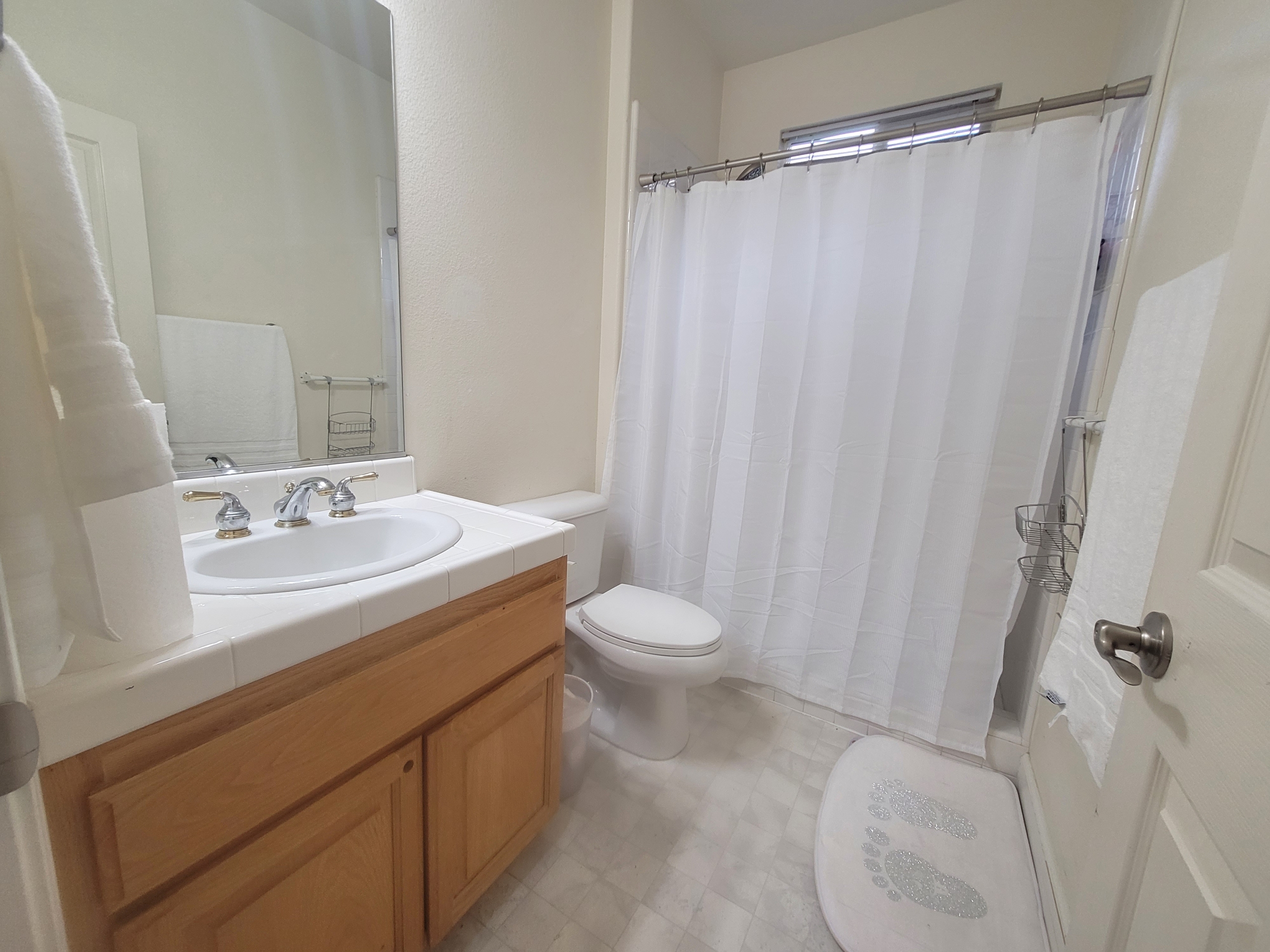 A bathroom with white tile and wood cabinets.