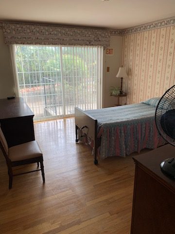 A bedroom with a bed, desk and fan.