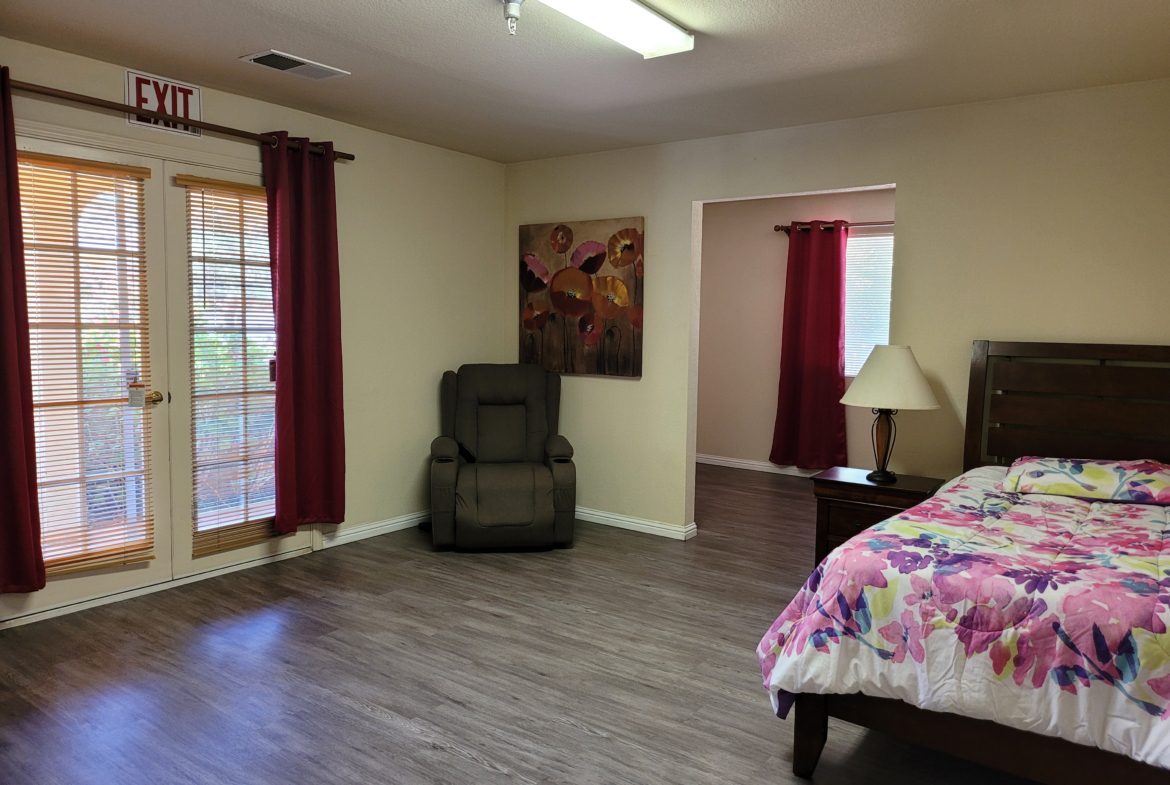 A bedroom with a bed, chair and table.