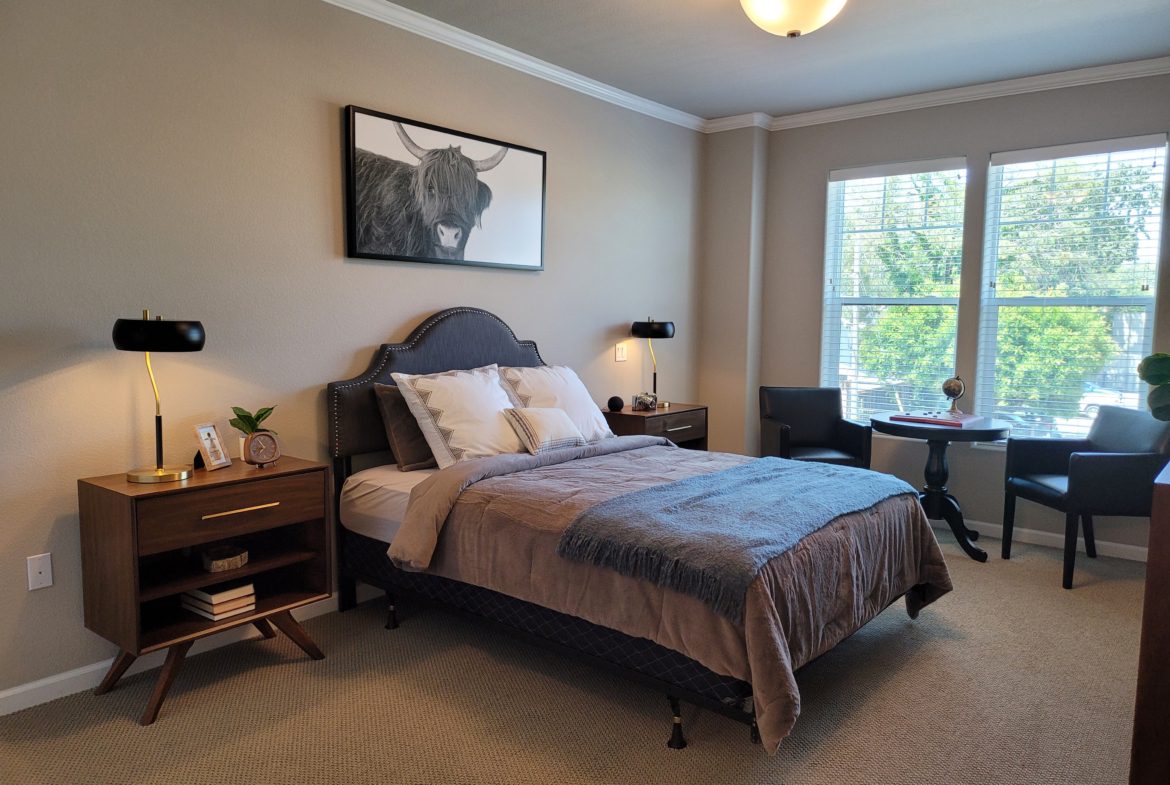 A bedroom with a bed, nightstand and desk.