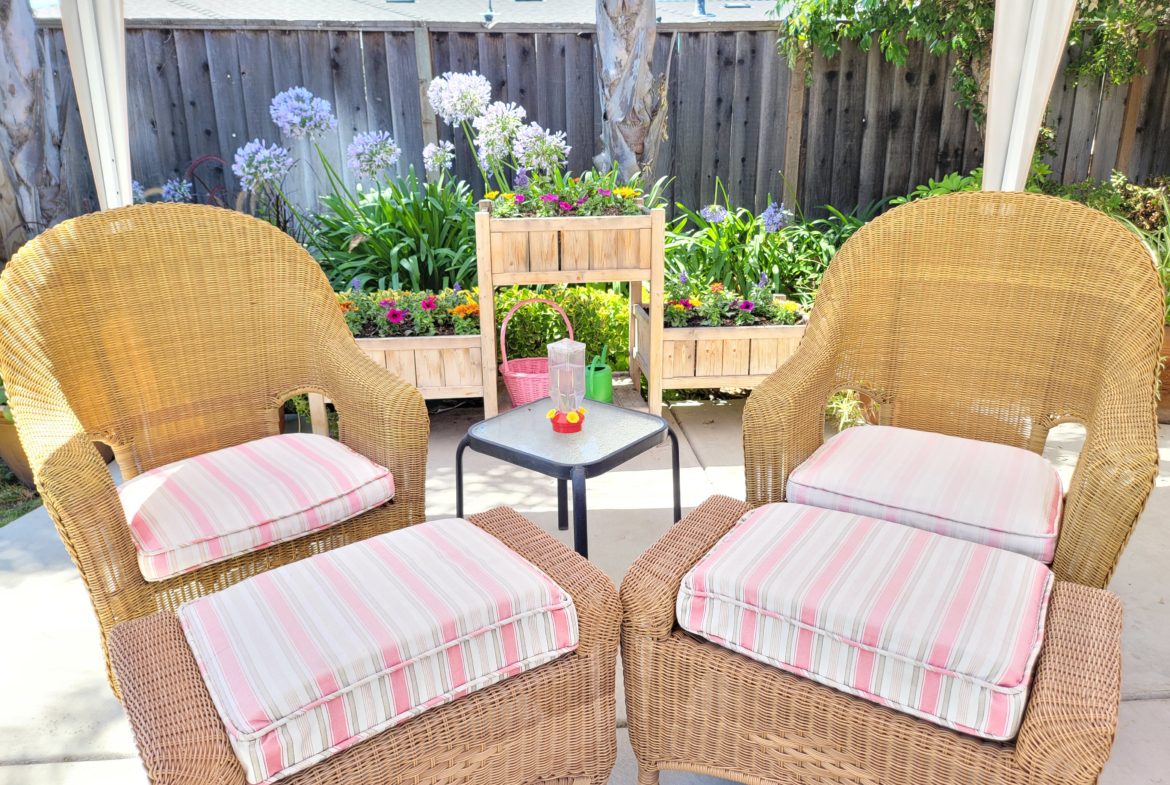 A patio with four chairs and ottomans on the ground.