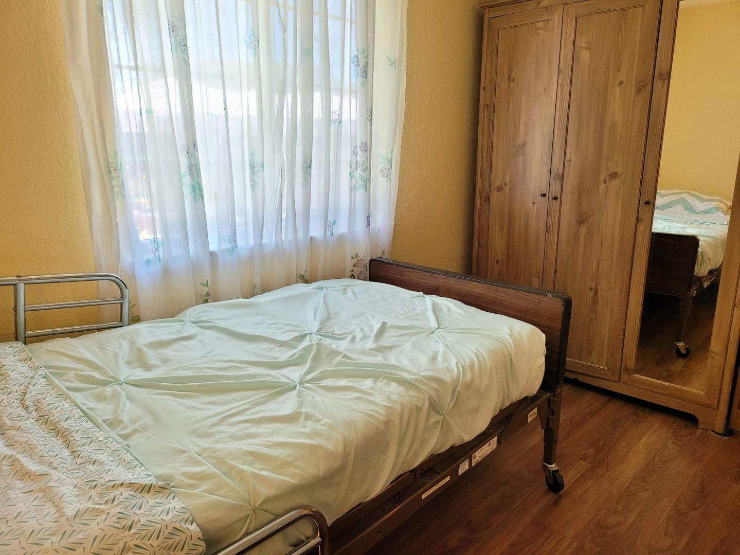 A bed room with a wooden floor and a white curtain