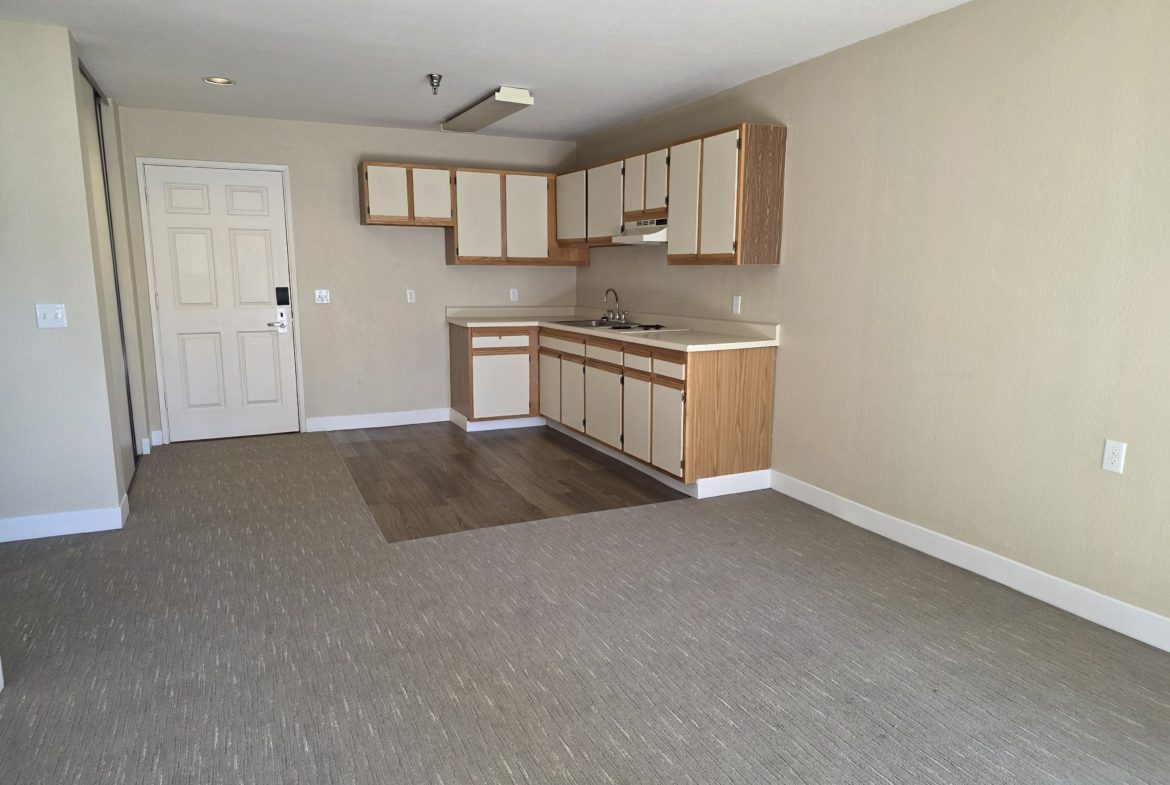 Empty room with kitchenette and carpet flooring.