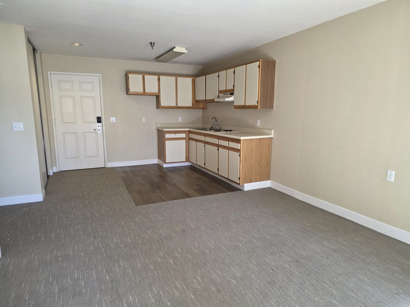 Empty room with kitchenette and carpet flooring.