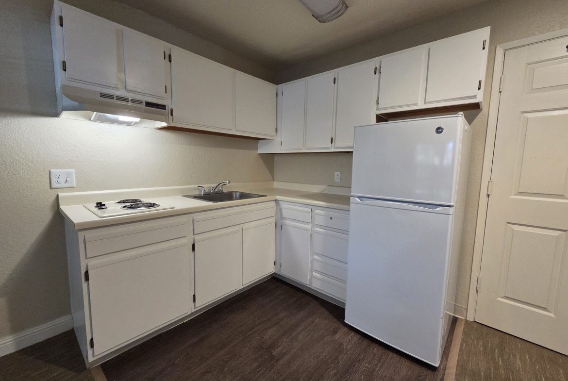 Small kitchen with white cabinets and fridge.