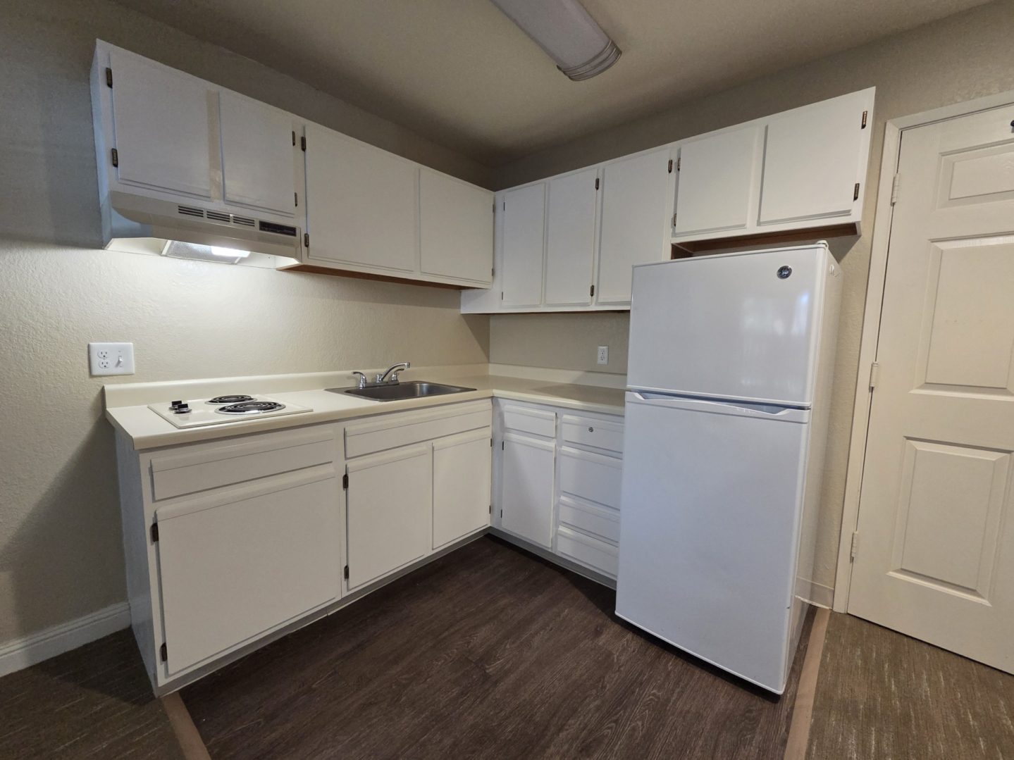 Small kitchen with white cabinets and fridge.